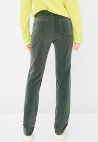 Samtgrüne Hose mit gerader Passform, ausgestattet mit zwei Gesäßtaschen und einer weichen Textur, kombiniert mit weißen Sneakers.