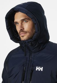 Chaqueta de pluma navy con collar alto y capucha ajustable. Incluye cremallera frontal, logotipo en el pecho y tejido texturizado. Ligera e aislante.