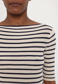Haut en tricot rayé avec des couleurs marine et crème, doté d'un col bateau et de manches courtes. Texture douce et design ajusté.