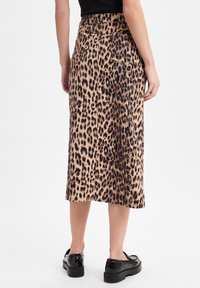 Leopardenmuster Midi-Rock aus einem braunen Stoff, mit hoher Taille, seitlichen Taschen und gerader Silhouette, kombiniert mit schwarzem Schuhwerk.