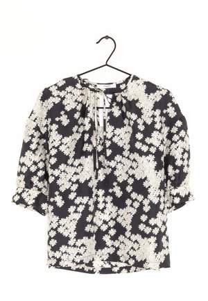 Czarna bluzka z białym kwiecistym wzorem, lekka tkanina, okrągły dekolt z wiązaniami, półdługie rękawy i falbaniaste akcenty.