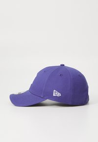 Gorra de béisbol morada con visera curva, hecha de tela, que presenta logotipos bordados en blanco en la parte frontal y lateral, y ojales de ventilación.