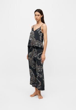 Jeune femme debout pieds nus portant un ensemble de pyjama noir ample avec un grand imprimé léopard et de fines bretelles sur le haut.