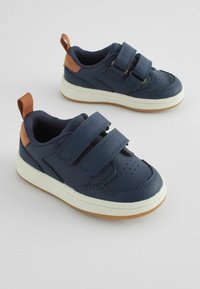 Baskets bleu marine avec deux straps Velcro, semelles en caoutchouc blanches et accents marron au talon. Elles disposent d'une boîte à orteils perforée et d'un matériau texturé.