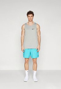 Grijze fitness tanktop met een zwart Nike-logo, gecombineerd met heldere turquoise sportshorts. Draagt witte sokken en sportschoenen.