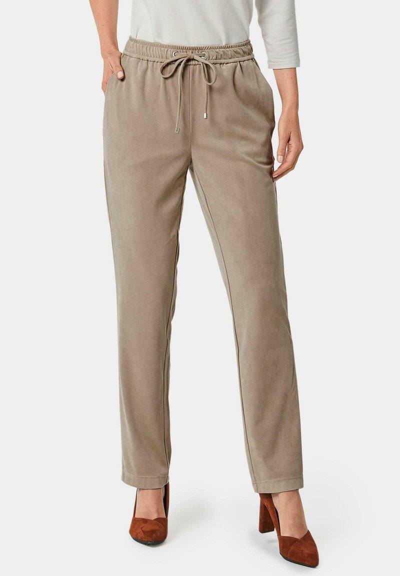 Beige loungebroeken met drawstring, zijzakken, taps toelopende pijpen en een zachte textuur, gecombineerd met bruine hoge hakken.