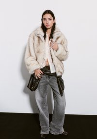 Cream faux fur jacket with oversized sleeves, light shirt underneath, gray wide-leg jeans, black leather bag tied around the waist.