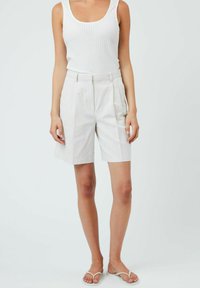 Weiße Leinen-Shorts mit maßgeschneidertem Schnitt, mit Falten, Seitentaschen und hoher Taille. Kombiniert mit einem figurbetonten weißen Rippen-Tanktop.