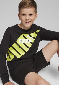 Czarna bluza z dużym żółtym logo "PUMA" i graficznym wzorem, w połączeniu z czarnymi szortami; materiał bawełniany, okrągły dekolt, luźny krój.