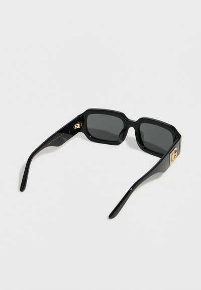 Μαύρα ορθογώνια γυαλιά ηλίου με σκουρόχρωμους φακούς και χρυσό διακοσμητικό λογότυπο στα μπράτσα του σκελετού, τοποθετημένα σε λευκό φόντο.