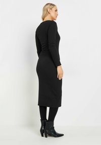 Vestido negro de manga larga acanalado con silueta ajustada, largo hasta la rodilla y cuello redondo, combinado con botas negras hasta el tobillo y leggins.