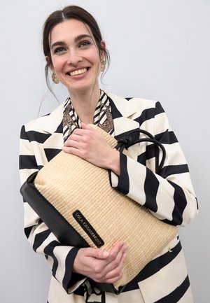 Bolso tote de paja trenzada con base plana, detalles en cuero negro y asas redondas; incluye una placa con el logo; forma rectangular en general.