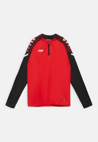 Rode sporttop met lange mouwen, zwarte onderkant, rits tot kwart nek en contrasterend schouderontwerp met stippen. Logo "JAKO" op de voorkant.
