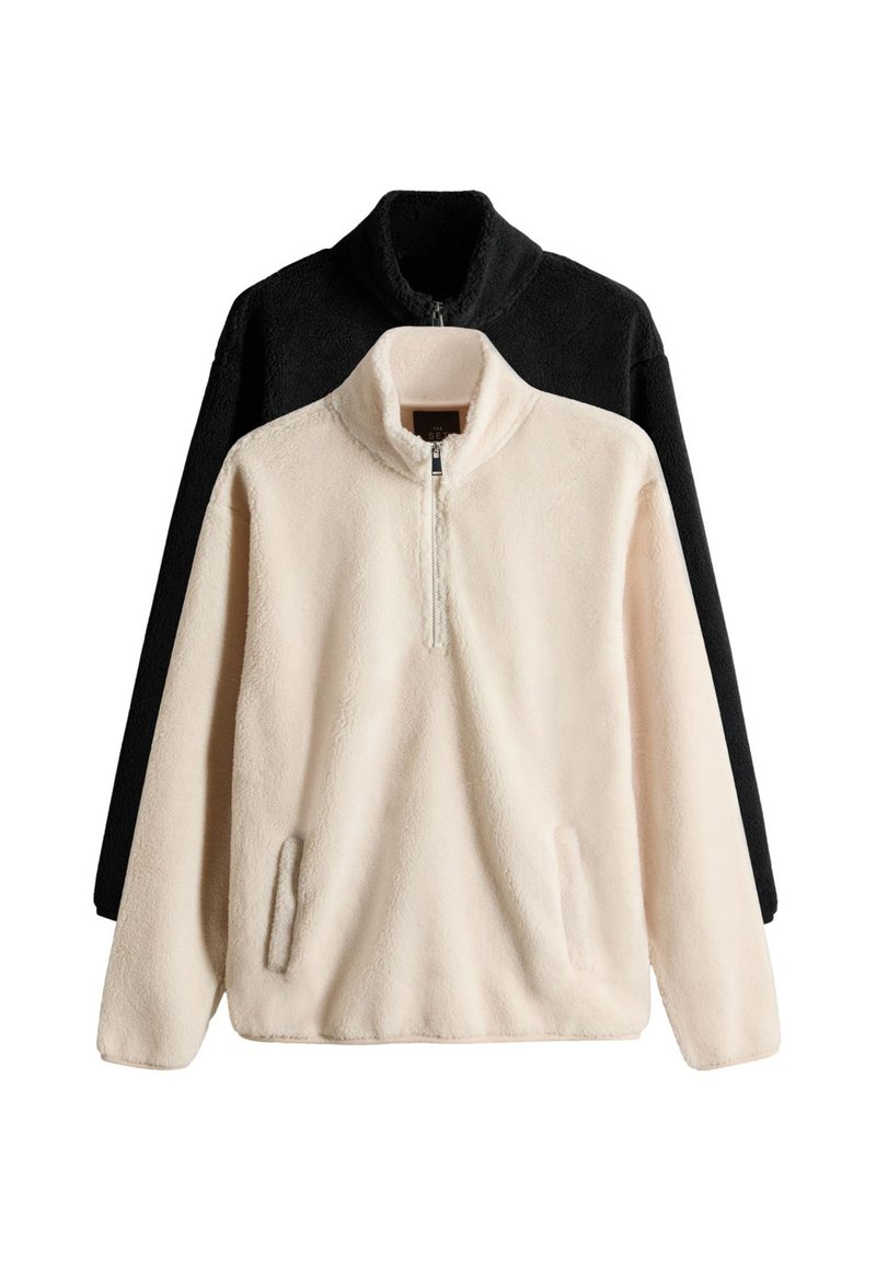 Dwa polarowe bluzy typu pullover, jedna w kremowym kolorze z zamkiem do połowy i bocznymi kieszeniami, druga w czarnym, obie miękkie i o fakturowanej powierzchni.