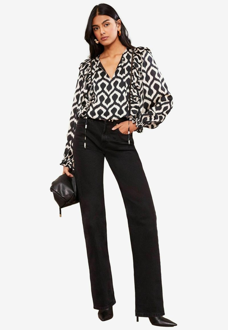 Blusa a righe in bianco e nero con maniche a volant abbinata a jeans neri a vita alta; la modella tiene una borsa nera e indossa tacchi a punta.