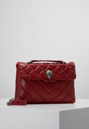 Bolso de cuero rojo acolchado con broche plateado en forma de mano, asa superior y correa desmontable, exhibido sobre un pedestal blanco.