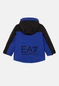 Μπλε και μαύρο μπουφάν με κουκούλα και μακριά μανίκια, φFeaturing μεγάλο μαύρο λογότυπ�ο "EA7 Emporio Armani" στην πλάτη.