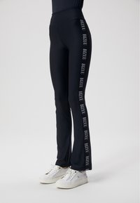 Zwarte legging met hoge taille en uitlopende ontwerp, voorzien van witte "BIZUU" merknaam langs de zijkanten, gemaakt van rekbare stof.