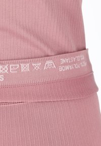 Tessuto a coste rosa chiaro con vita elastica, caratterizzato da simboli di cura e nome del marchio in bianco. Texture liscia con un design aderente.