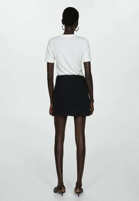 Black textured mini skirt paired with a fitted white t-shirt. The skirt features a high waist and a simple design.
