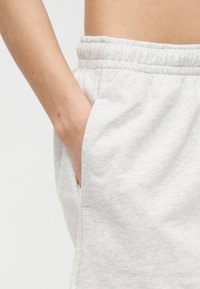 Το αριστερό χέρι εισάγεται στην πλαϊνή τσέπη γκρι ανοιχτού χρώματος φόρμας με ελαστική μέση, που φοριέται από ένα άτομο με γυμνή κοιλιά.