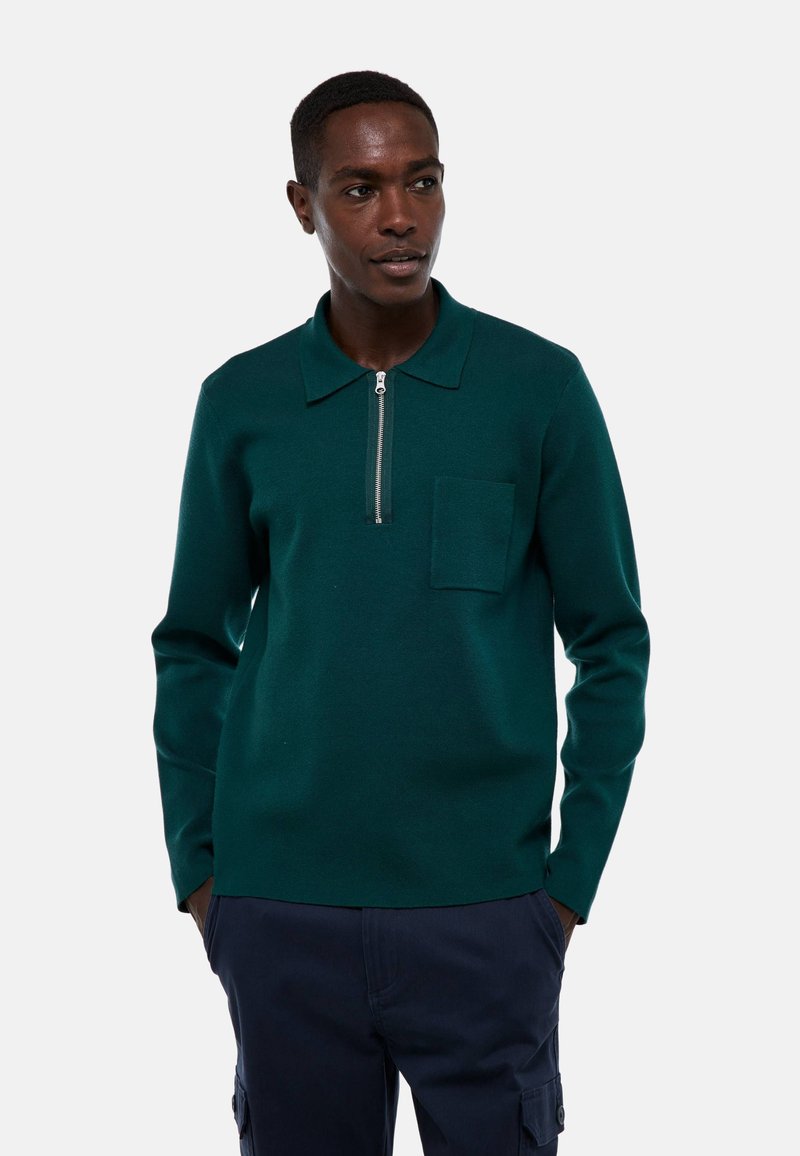 Pull en maille vert foncé avec un col, fermeture éclair quart de zip à l'avant, et une poche sur la poitrine. Texture lisse et manches longues ajustées.