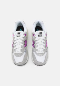 Paire de baskets New Balance 580 en gris et blanc avec logos violets, lacets blancs et semelles intérieures noires, vues de dessus.
