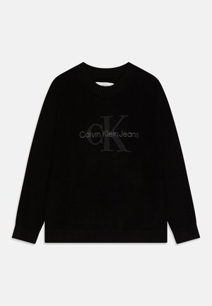 Suéter negro acanalado con cuello redondo, que presenta un logo gris de "Calvin Klein Jeans" en el centro. Manga larga y tejido texturizado.