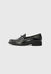 Mocassins en cuir verni noir avec un bout rond, un talon bas et un matériel en métal décoratif à l'avant. Texture lisse, design minimal.