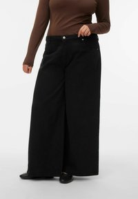 Zwarte wijde jeans van denim, met een hoge taille, knoop- en ritssluiting, en twee voorzakken. De stof heeft een gladde textuur.