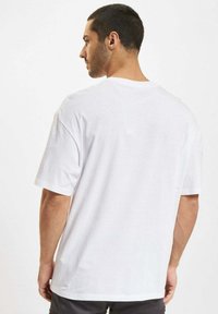 T-shirt bianco in cotone con maniche corte, vestibilità rilassata, collo a giro, senza motivi o grafiche visibili, mostrato da dietro.