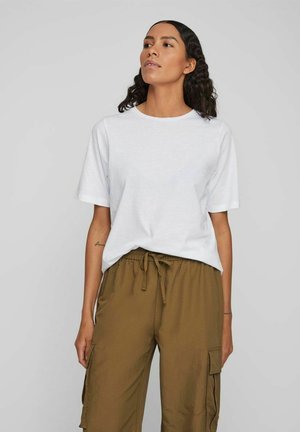 Weißes Baumwoll-T-Shirt mit kurzen Ärmeln, kombiniert mit braunen Cargo-Hosen mit Seitentaschen und elastischem Bund. Einfaches Design und Passform.