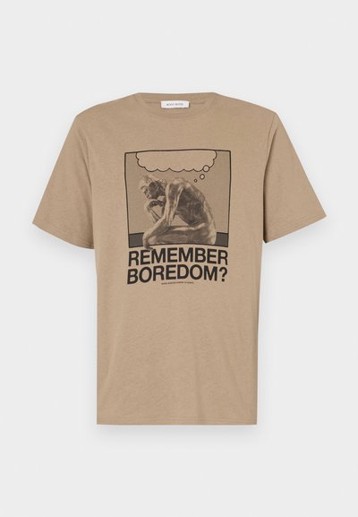 T-shirt en coton beige avec un graphique représentant une figure en train de réfléchir et le texte "TU TE SOUVIENS DE L'ENNUI ?" imprimé en noir. Design à col ras du cou.