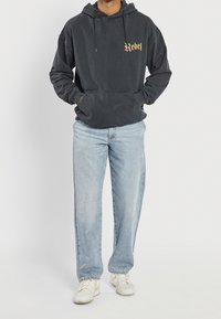 Mørkegrå hættetrøje med et "Rebel"-motiv i mange farver. Kombineret med lyseblå jeans med lige ben og hvide sneakers.