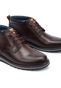 Brown leather ankle boots with a smooth finish, lace-up front, metal eyelets, and contrasting cushioned collar. Rubber sole with stitching detail.