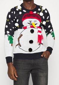 Gestrickter Weihnachtspullover mit einem Schneemann-Motiv. Dunkelblauer Hintergrund, weiße Schneeflocken und farbenfrohe Akzente, darunter ein rotes Hut und ein Schal.