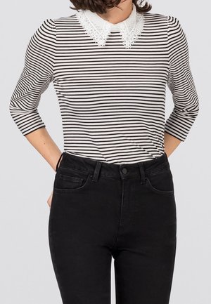 Schwarz-weiß gestreiftes Oberteil mit Spitzkragen, kombiniert mit hoch taillierter schwarzer Jeans. Verfügt über Dreiviertelärmel und eine taillierte Passform.