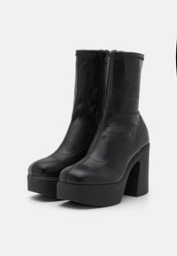 Las botas de tobillo de cuero negro presentan una superficie lisa, punta redondeada y un tacón de plataforma grueso. Cierre con cremallera lateral para ponerlas y quitarlas fácilmente.