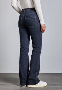 Jeans rectos de mezclilla en azul oscuro, con bolsillos traseros, una etiqueta negra en la cintura y combinados con zapatillas blancas.