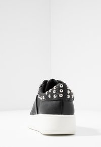 Musta nahkakengät, joissa on teksturoitu musta yksityiskohta ja hopeiset niitit takaosassa. Varustettu valkoisella kumipohjalla ja tasaisella designilla.