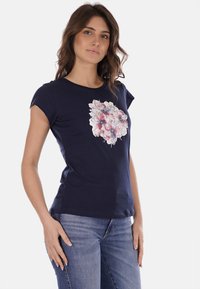 T-shirt di cotone blu navy con maniche corte, caratterizzata da una stampa floreale bianca e rosa davanti. Design aderente, texture morbida.