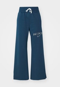Mörkblå vida sweatpants med ribbad elastisk midja, vit dragsko och vit Nike-logga på höger lår.