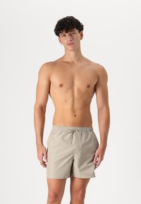 Shorts de bain beige clair en tissu lisse, dotés d'une taille élastique avec cordon de serrage. Longueur au-dessus du genou sans motifs.