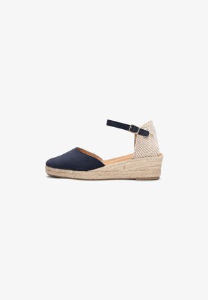 Sandalia cuña espadrille de punta cerrada en azul marino con tacón tejido beige, correa en el tobillo y cierre de hebilla sobre fondo blanco.