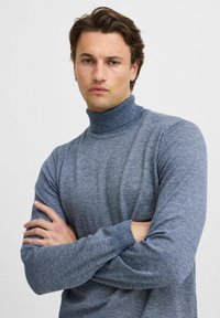 Modra pulover s turtleneck ohlapnega kroja, izdelan iz mehkega pletenega materiala, z teksturo in rebrastimi manšeti, prilagojene silhuete in dolgimi rokavi.