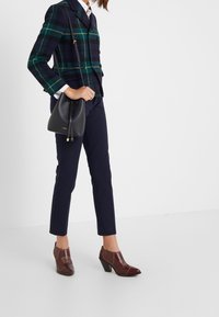 Marynarka w kratę w niebieskich i zielonych odcieniach, granatowe spodnie oraz brązowe botki na obcasie z teksturowanymi detalami. Występuje czarna torebka typu bucket.