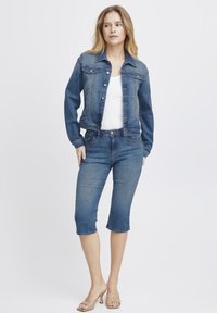 Denim jakna z gumbom za zapiranje, prilega se telesu, svetlo obdelava in dva žepa na prsih; v kombinaciji z jeans hlačami do sredine stegen v temnejši obdelavi.