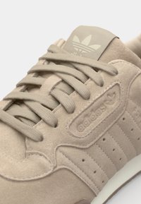 Beige velur copati z ravnimi vezalkami, teksturiranim zgornjim delom in tremi črtami. Ima logotip na ježku in bel podplat.