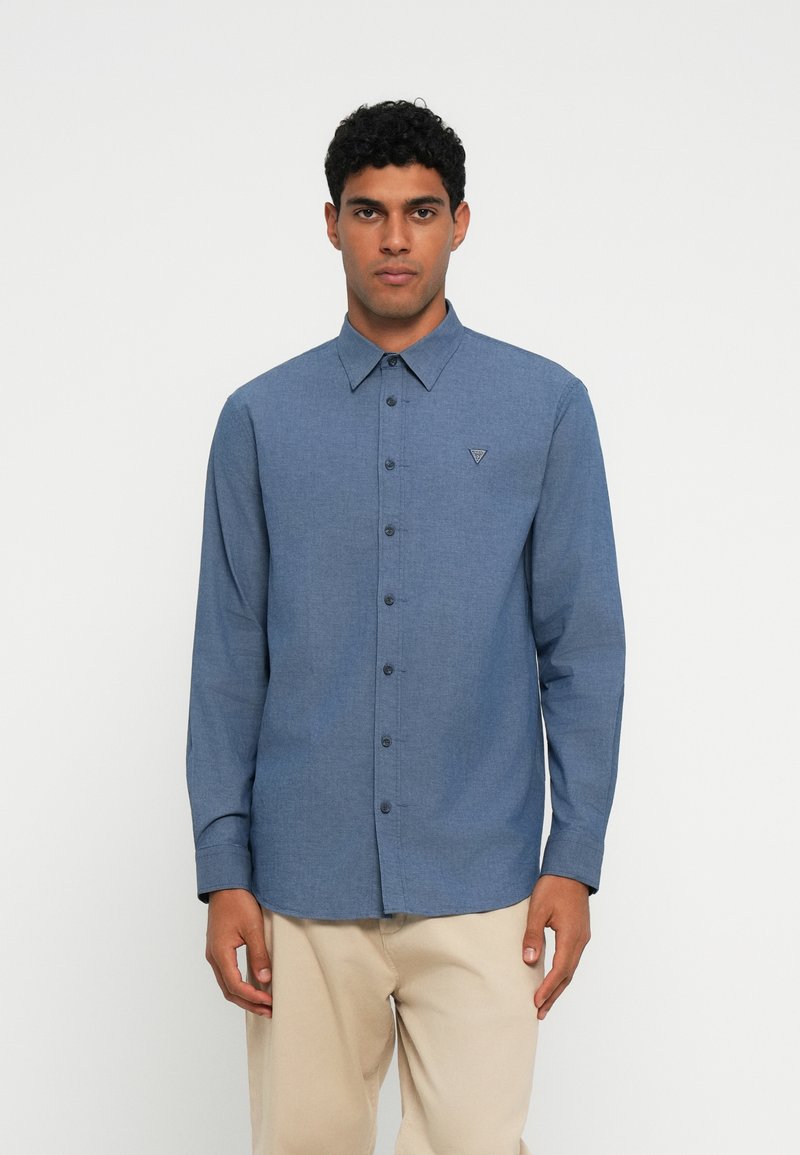 Camicia a maniche lunghe con bottoni in tessuto blu mélange. Presenta un col a punta, logo sul petto e orlo dritto. Design semplice, senza motivi.