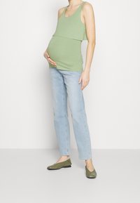 Grön ärmlös graviditetstopp med ett lagerdesign, kombinerad med ljusblå raka jeans och mörkgröna ballerinas. Enkelt och avslappnat utseende.